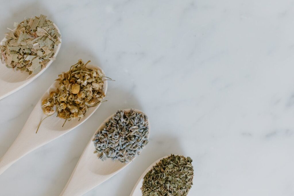 Flat lay of dried herbs in spoons for aromatherapy on white background.